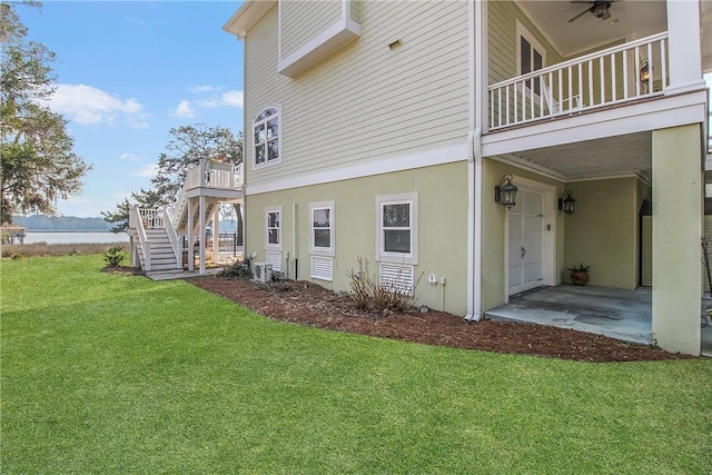 view of side of property featuring stucco siding, a water view, a lawn, an attached garage, and stairs