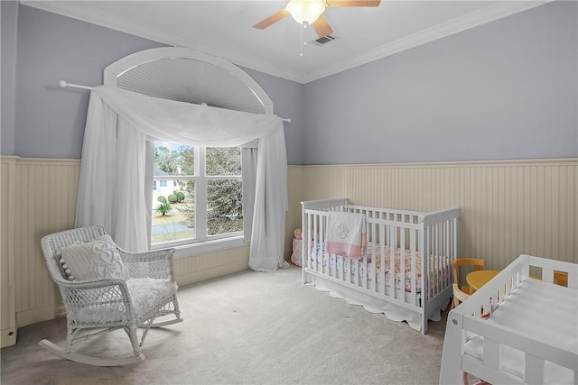 carpeted bedroom with a wainscoted wall, a ceiling fan, crown molding, and visible vents