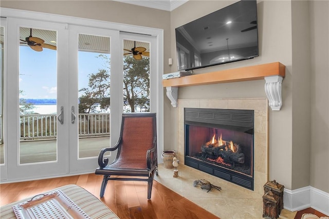 living area with ornamental molding, a tile fireplace, ceiling fan, and wood finished floors