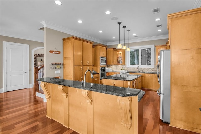 kitchen with dark wood-type flooring, a sink, arched walkways, appliances with stainless steel finishes, and brown cabinetry