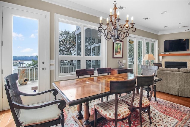 dining area with light wood-type flooring, visible vents, a fireplace, and crown molding