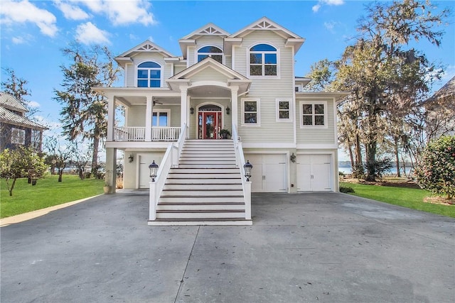 raised beach house featuring stairway, covered porch, ceiling fan, concrete driveway, and a garage