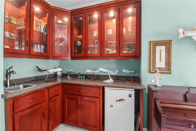 kitchen featuring dark countertops, glass insert cabinets, fridge, and a sink