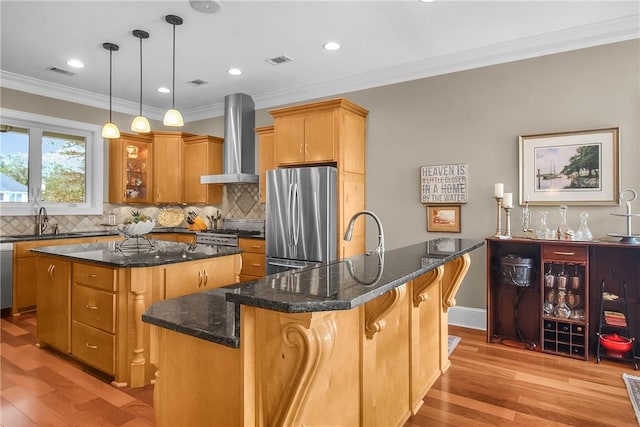 kitchen featuring visible vents, a center island with sink, appliances with stainless steel finishes, wall chimney exhaust hood, and a sink