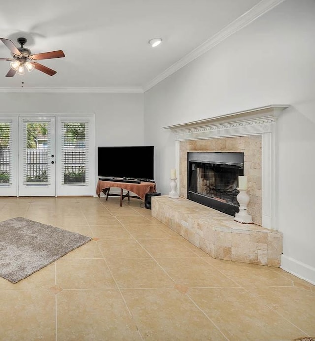 tiled living room with french doors, ceiling fan, ornamental molding, and a tiled fireplace