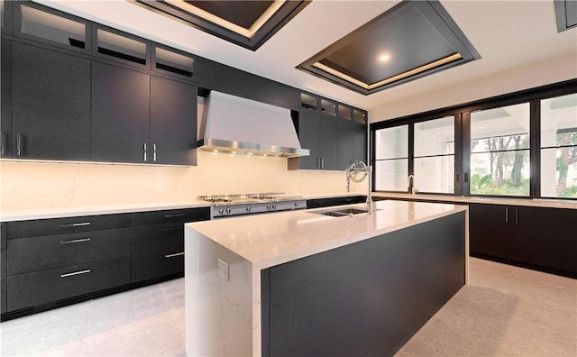 kitchen featuring a center island with sink, wall chimney range hood, sink, and stainless steel gas cooktop