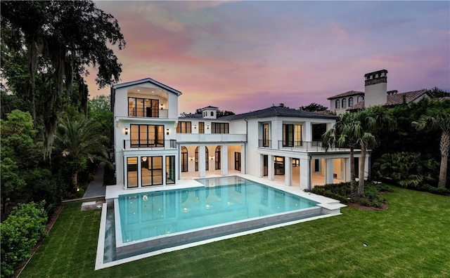 back house at dusk with a yard, a patio area, and a balcony