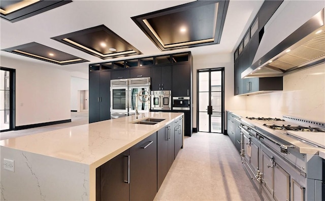 kitchen with wall chimney range hood, sink, light stone countertops, a large island, and stainless steel appliances