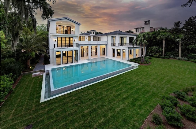 back house at dusk with a lawn, a balcony, and a patio