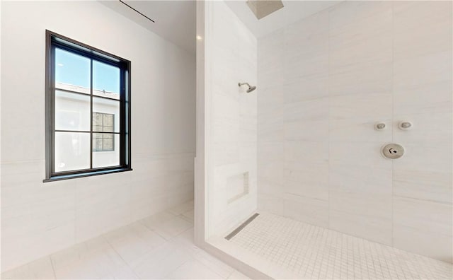 bathroom featuring tile patterned flooring, a tile shower, and tile walls