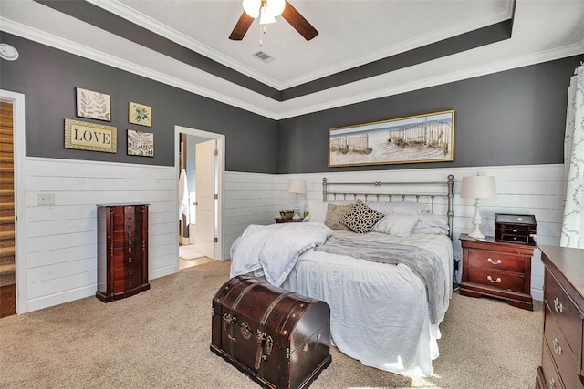 carpeted bedroom with visible vents, a raised ceiling, a ceiling fan, and wainscoting