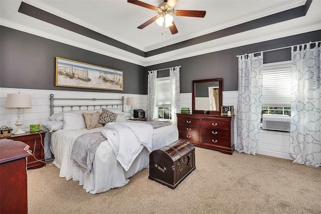 carpeted bedroom with cooling unit, a wainscoted wall, ceiling fan, crown molding, and a raised ceiling