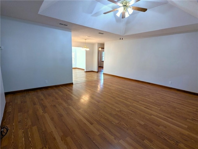 empty room featuring vaulted ceiling, dark wood-type flooring, and ceiling fan with notable chandelier