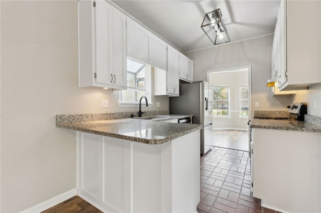 kitchen with white cabinetry, sink, kitchen peninsula, dark stone countertops, and crown molding