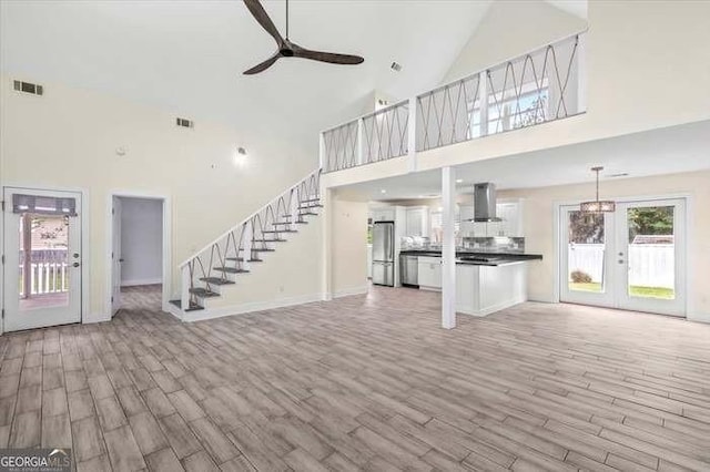 unfurnished living room with french doors, light wood-type flooring, high vaulted ceiling, and ceiling fan