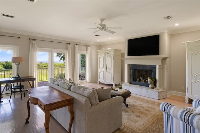 living room featuring light hardwood / wood-style floors, ceiling fan, ornamental molding, and a tiled fireplace