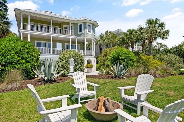 back of property featuring a balcony, a fire pit, and a lawn