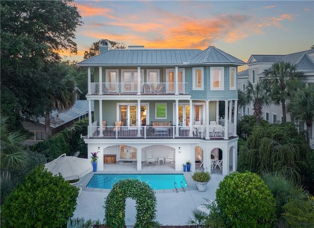 back house at dusk with a balcony, a patio, and french doors