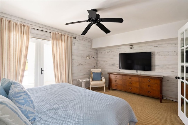 bedroom featuring french doors, light colored carpet, ceiling fan, and wooden walls