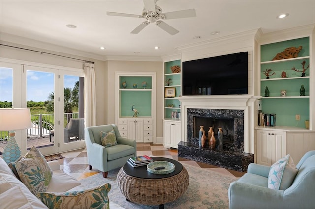 living room with a high end fireplace, ornamental molding, built in shelves, ceiling fan, and light hardwood / wood-style flooring