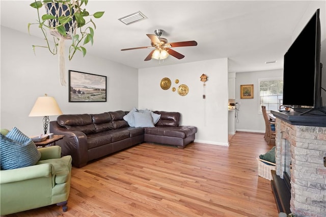 living room with a stone fireplace, ceiling fan, and light wood-type flooring