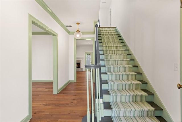 staircase with visible vents, crown molding, baseboards, a fireplace, and wood finished floors