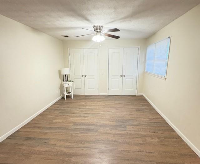 unfurnished bedroom featuring wood finished floors, baseboards, and two closets