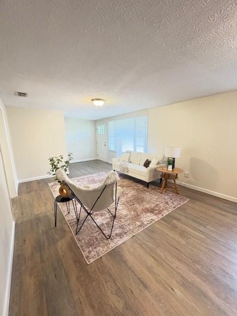 living room with visible vents, baseboards, a textured ceiling, and wood finished floors