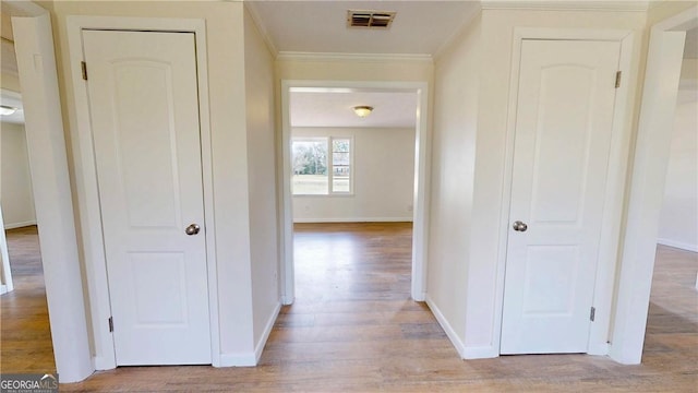 hall with visible vents, ornamental molding, baseboards, and light wood-type flooring