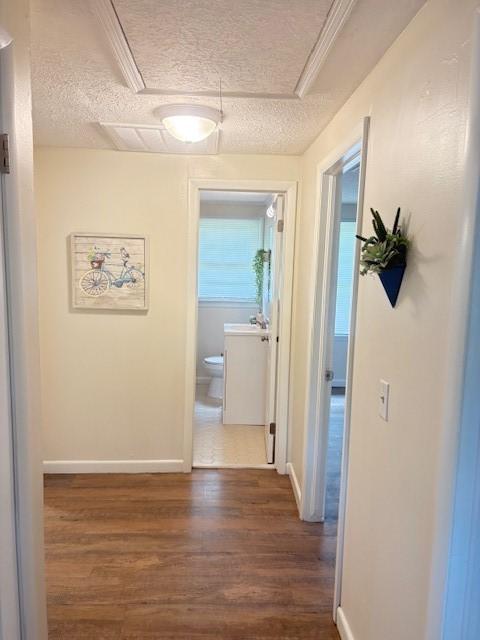 hall with a sink, baseboards, a textured ceiling, and dark wood-type flooring