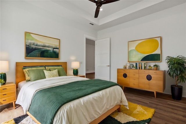 bedroom with ceiling fan, a raised ceiling, and dark wood-type flooring