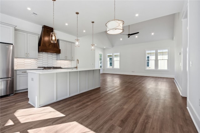 kitchen with hanging light fixtures, dark hardwood / wood-style floors, a center island with sink, custom exhaust hood, and appliances with stainless steel finishes