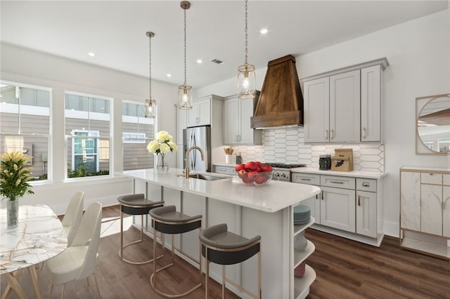 kitchen featuring appliances with stainless steel finishes, backsplash, dark wood-type flooring, sink, and an island with sink