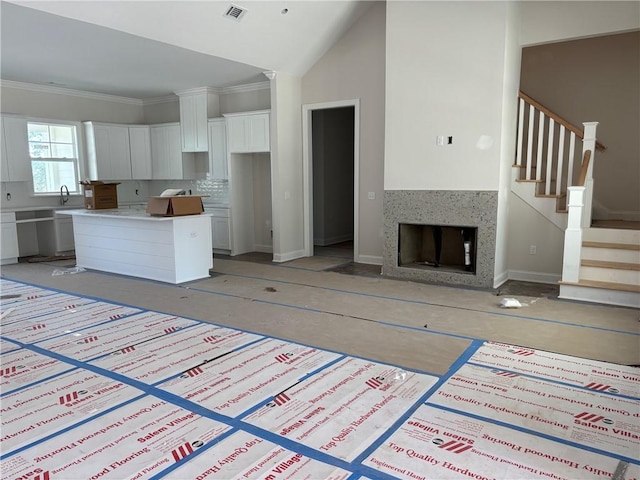 kitchen with lofted ceiling, ornamental molding, a kitchen island, white cabinets, and backsplash