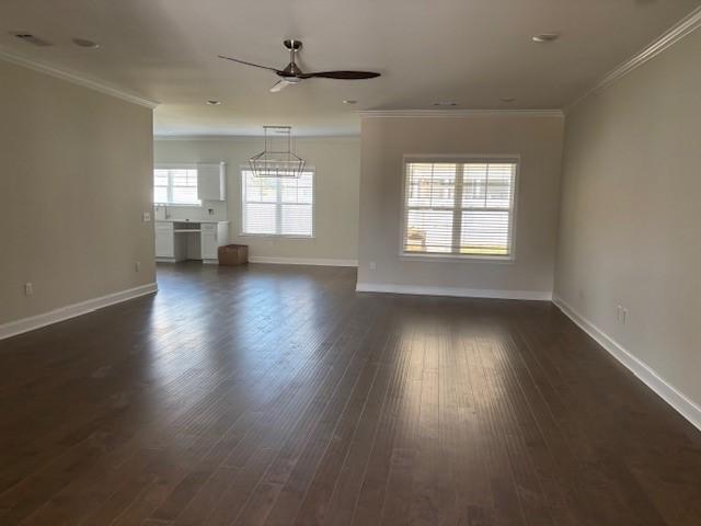 unfurnished living room with baseboards, ceiling fan, ornamental molding, and dark wood-style flooring