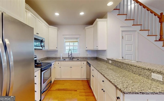 kitchen with white cabinetry, light stone countertops, sink, appliances with stainless steel finishes, and light wood-type flooring