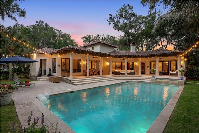 back of house at dusk featuring an outdoor pool, a patio, and a tile roof