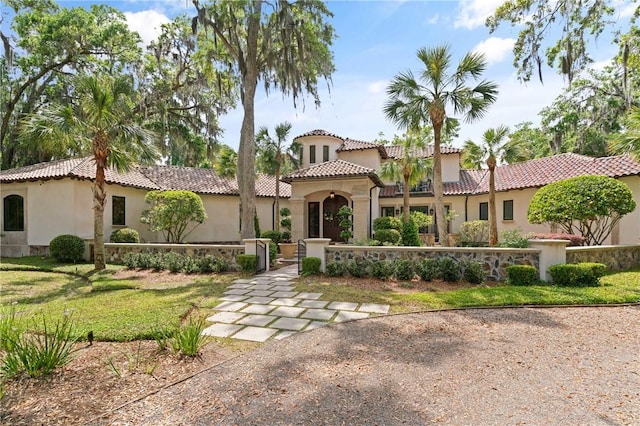 mediterranean / spanish-style house featuring stucco siding, a tiled roof, and a fenced front yard