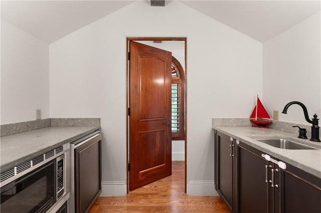 kitchen featuring stainless steel microwave, a sink, light wood-type flooring, baseboards, and lofted ceiling