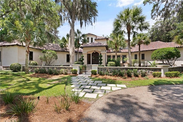 mediterranean / spanish-style home with a tile roof, a fenced front yard, a gate, and stucco siding