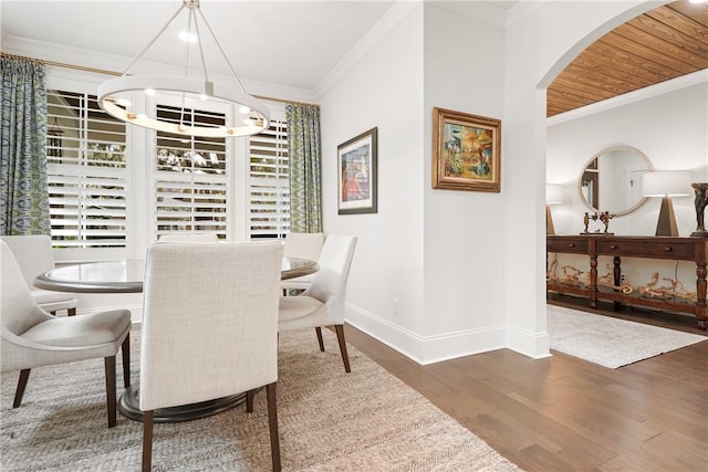 dining space with dark wood-type flooring, ornamental molding, and a notable chandelier