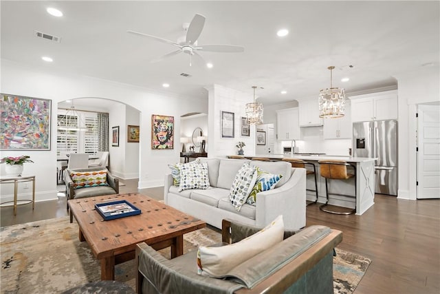 living room with crown molding, ceiling fan with notable chandelier, and dark wood-type flooring