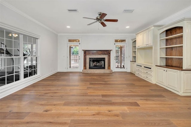 unfurnished living room featuring built in shelves, ceiling fan, ornamental molding, and light wood-type flooring