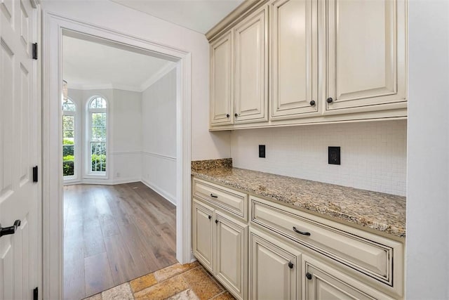 kitchen featuring light stone countertops, light wood-type flooring, tasteful backsplash, crown molding, and cream cabinetry