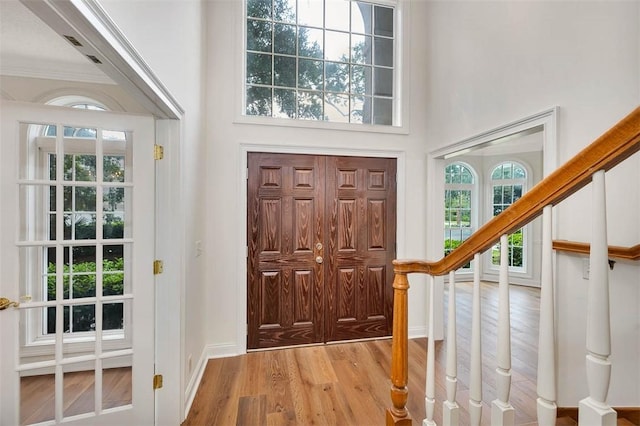 foyer entrance with light wood-type flooring, crown molding, and a towering ceiling