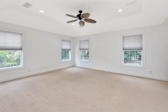 unfurnished room featuring a raised ceiling, light carpet, ceiling fan, and a healthy amount of sunlight