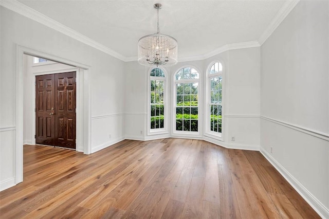 spare room with light wood-type flooring, an inviting chandelier, and ornamental molding