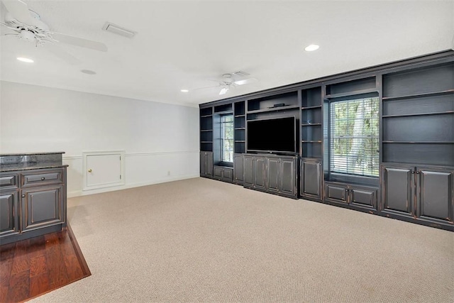 unfurnished living room with dark colored carpet, built in shelves, and ceiling fan