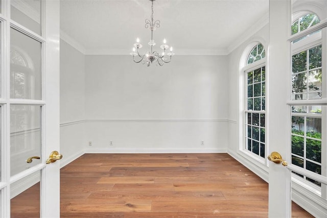 empty room with crown molding, a chandelier, and light hardwood / wood-style floors