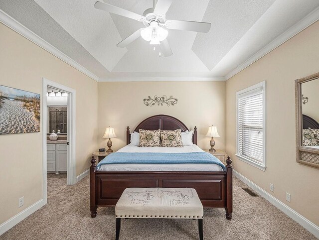 carpeted bedroom featuring a tray ceiling, ensuite bath, ceiling fan, and ornamental molding